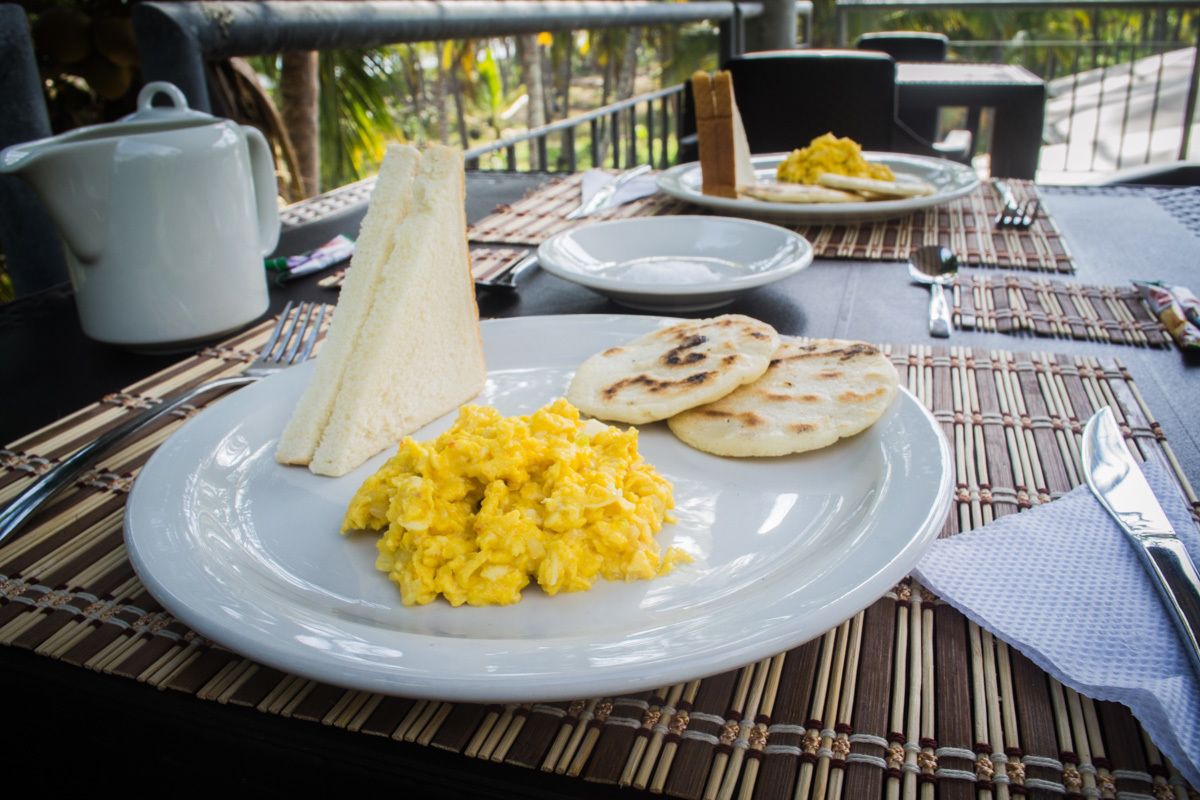 A dining table with a plate of scrambled eggs, flatbread, and a white cup.