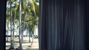 A view through a window with curtains, featuring palm trees and a beach. - Tayrona Tented Lodge (Santa Marta)
