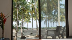 A room with a large window overlooking a beach with palm trees. - Tayrona Tented Lodge (Santa Marta)