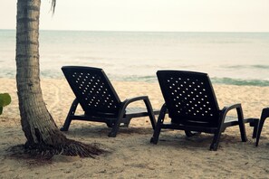 Two black lounge chairs on a sandy beach with a palm tree and ocean view. - Tayrona Tented Lodge (Santa Marta)