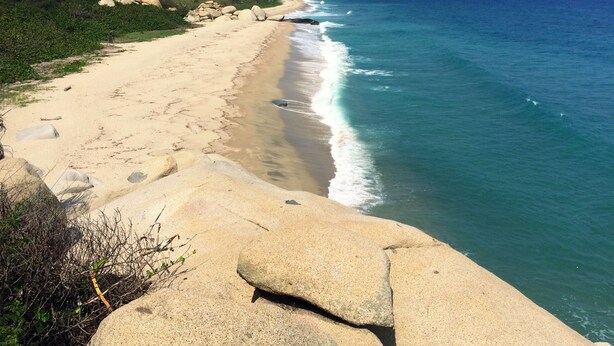 A coastal landscape with a sandy beach, rocky outcrops, and a clear view of the ocean. - Tayrona Tented Lodge (Santa Marta)