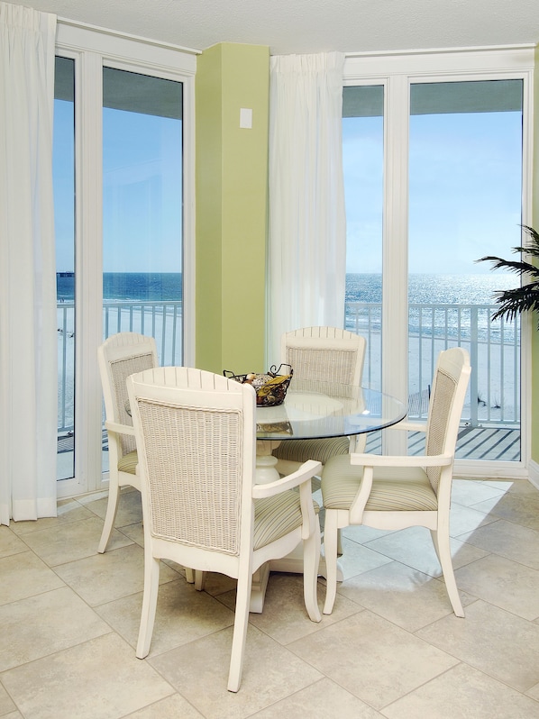 Un comedor con mesa de vidrio y sillas de mimbre, con vista a una playa y un muelle.