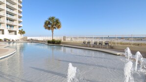 Una piscina con chorros de agua, una palmera y una valla con sillas de descanso.