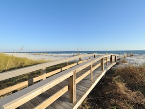 Un muelle de madera que conduce a una playa con arena y césped.