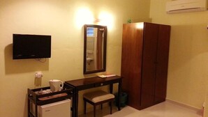 Ein kleines Hotelzimmer mit einem Holztisch, einem kleinen Kühlschrank, einem Fernseher, einem Spiegel und einem Kleiderschrank.
