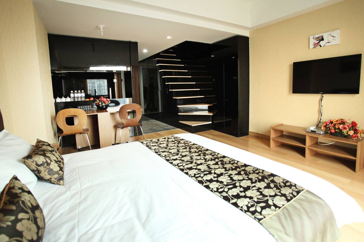 Een moderne hotelkamer met een groot bed, een bureau, een stoel, een televisie en een trap naar een hoger gelegen verdieping.