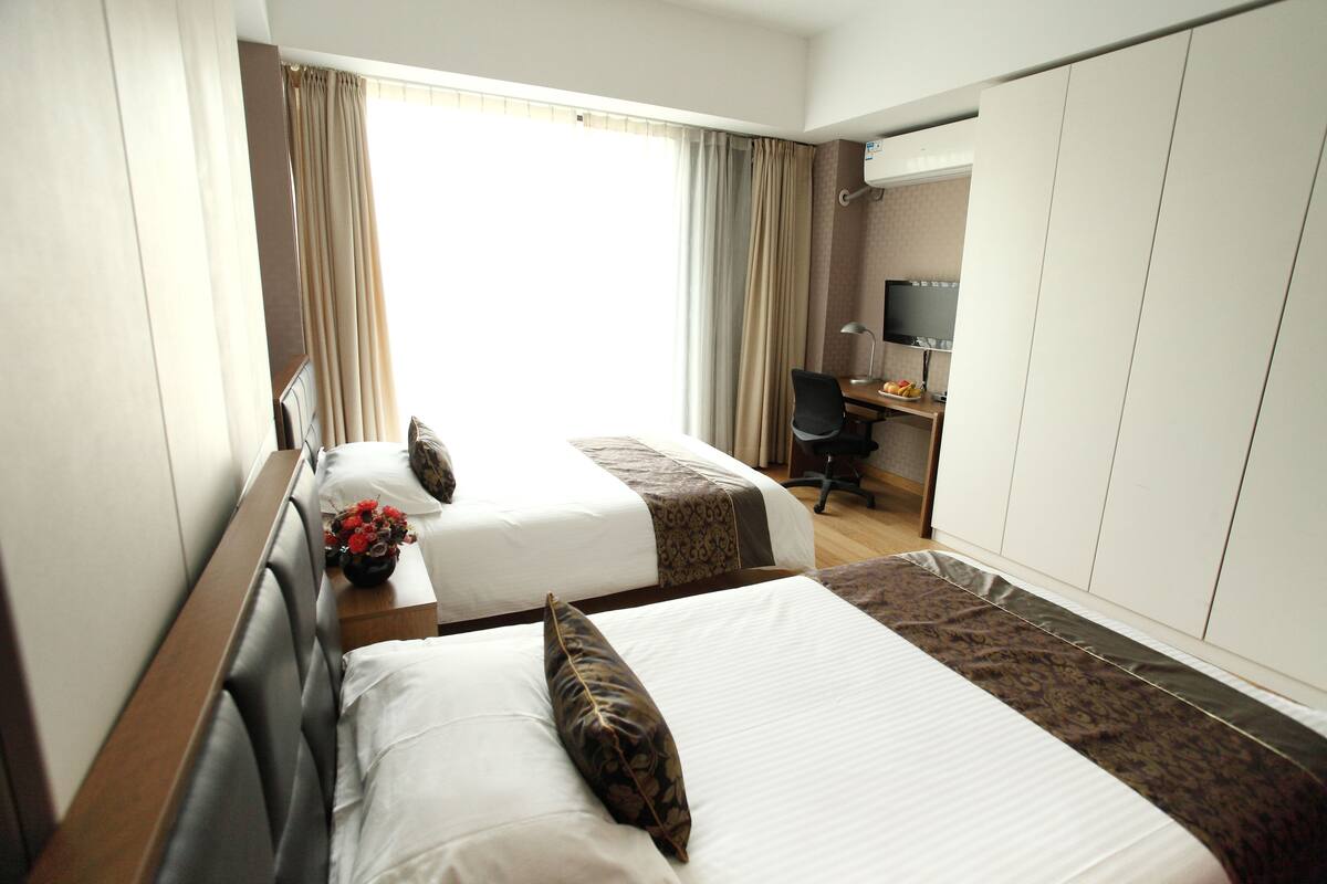 Een hotelkamer met twee bedden, een bureau, een televisie en een raam met gordijnen.