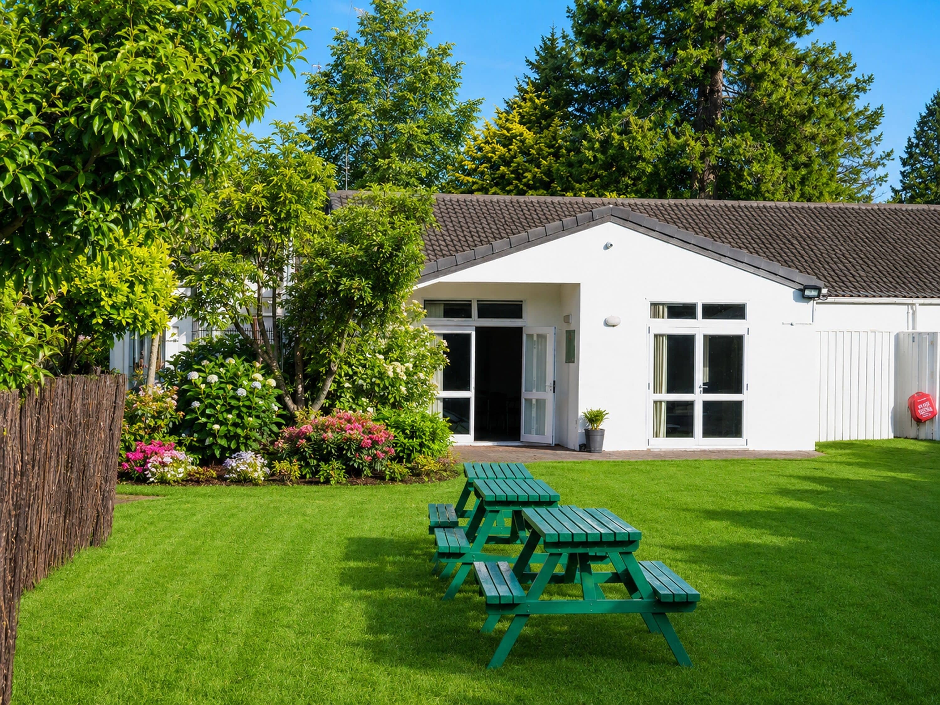 A white building with a tiled roof, a green picnic table, and a well-maintained lawn.