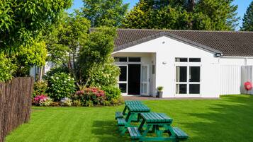 A white building with a tiled roof, a green picnic table, and a well-maintained lawn.
