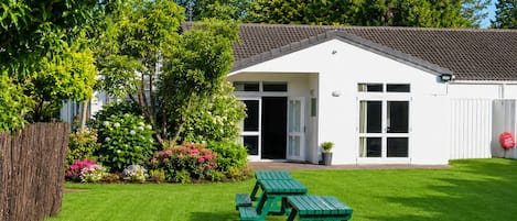 A white building with a tiled roof, a green picnic table, and a well-maintained lawn.