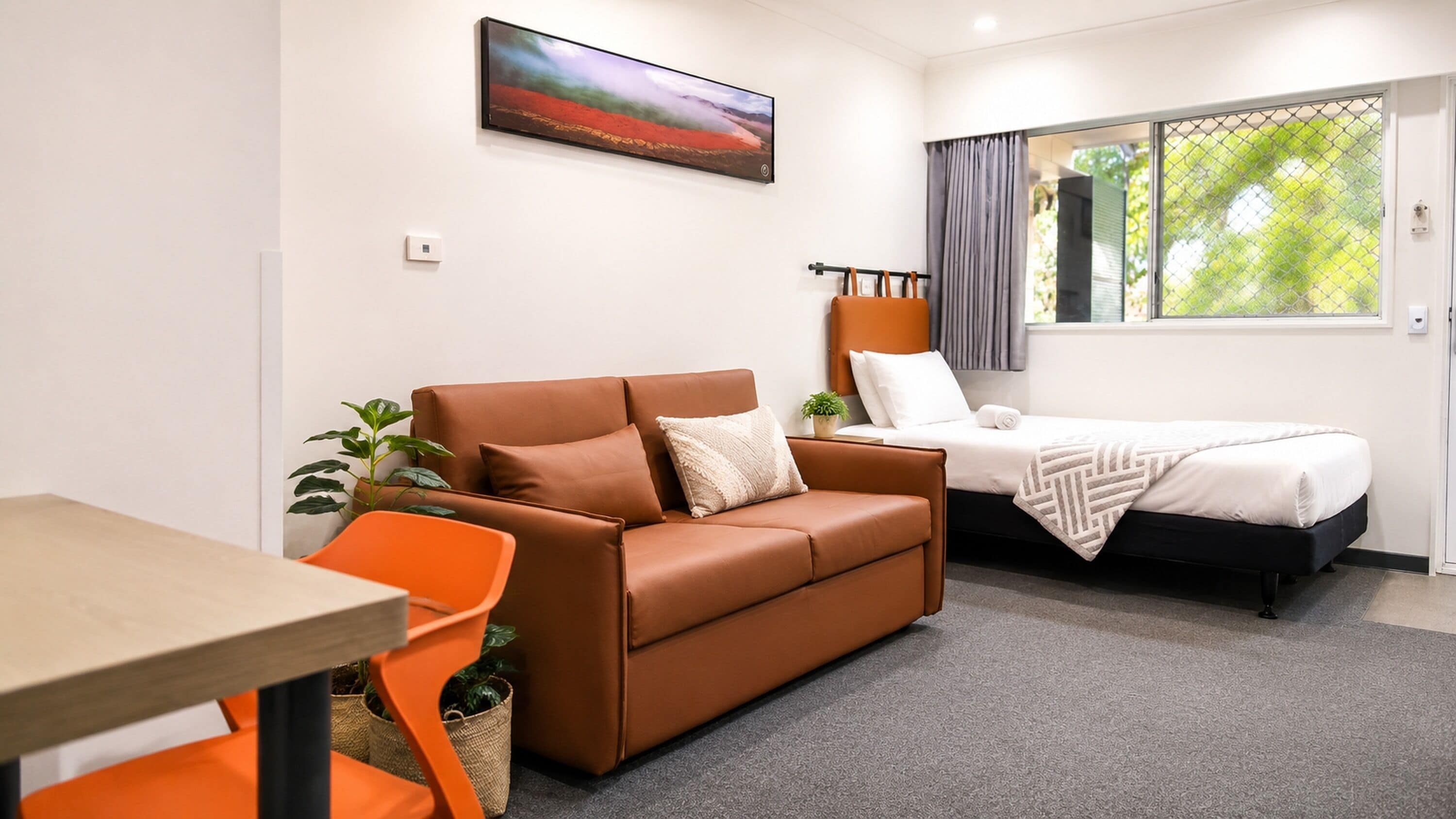 A modern room with a brown sofa, a small table, a single bed, and a window with curtains.