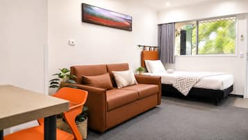 A modern room with a brown sofa, a small table, a single bed, and a window with curtains.