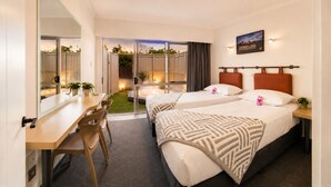 A hotel room with two beds, a desk, chairs, a small balcony, and a view of the outdoors. - Alpin Motel & Conference Centre (Rotorua)
