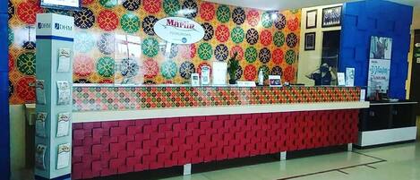 Un mostrador de recepción con una pared decorada con un patrón colorido, un cartel que dice "Marlin Pekalongan" y una pared azul con un cartel a la derecha.