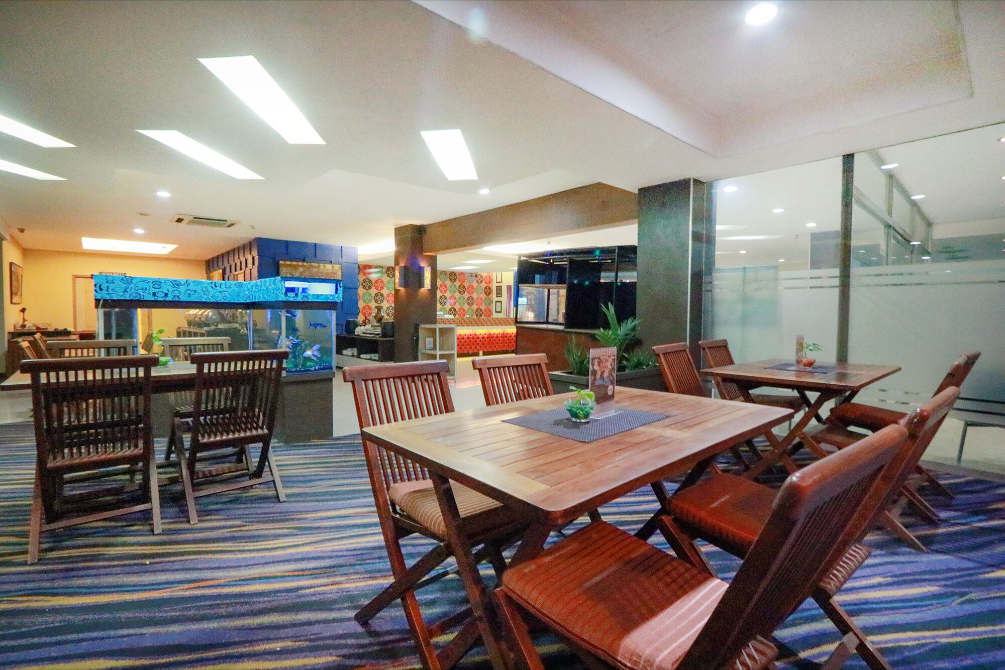 A restaurant with wooden tables and chairs, a fish tank, and a patterned carpet.