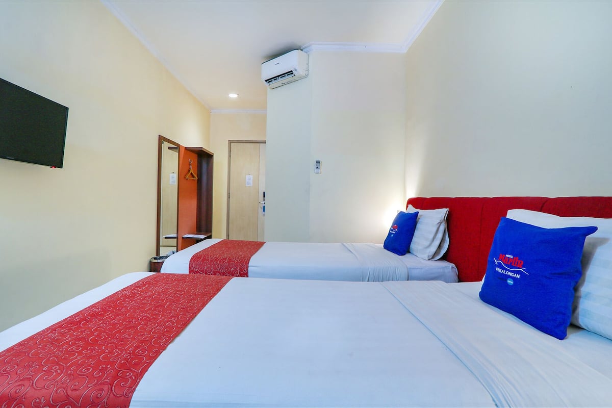 Une chambre d’hôtel avec deux lits, chacun agrémenté d’oreillers rouges et bleus, un téléviseur à écran plat fixé au mur et un appareil de climatisation installé au plafond.