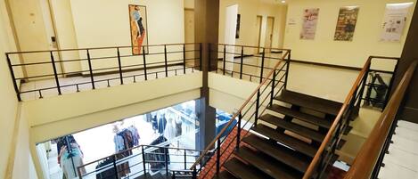 A multi-level interior with a central staircase, glass railings, and a view of a clothing store below.