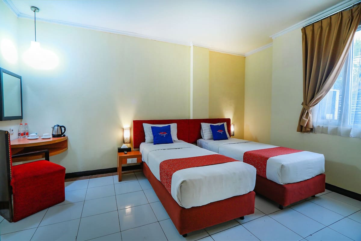 Une chambre d’hôtel avec deux lits simples, un bureau avec une chaise, une petite table avec une bouilloire et un miroir.