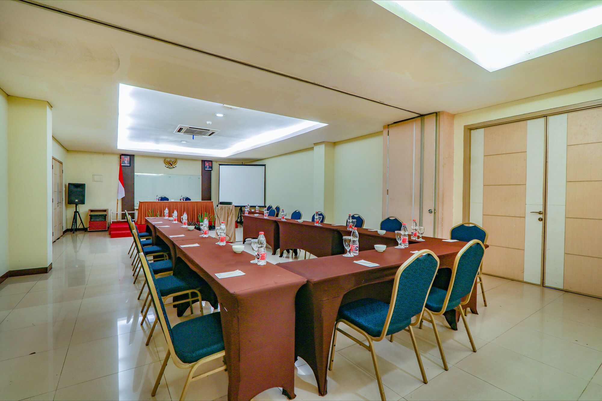 A conference room with a long table, blue chairs, and a projector screen.