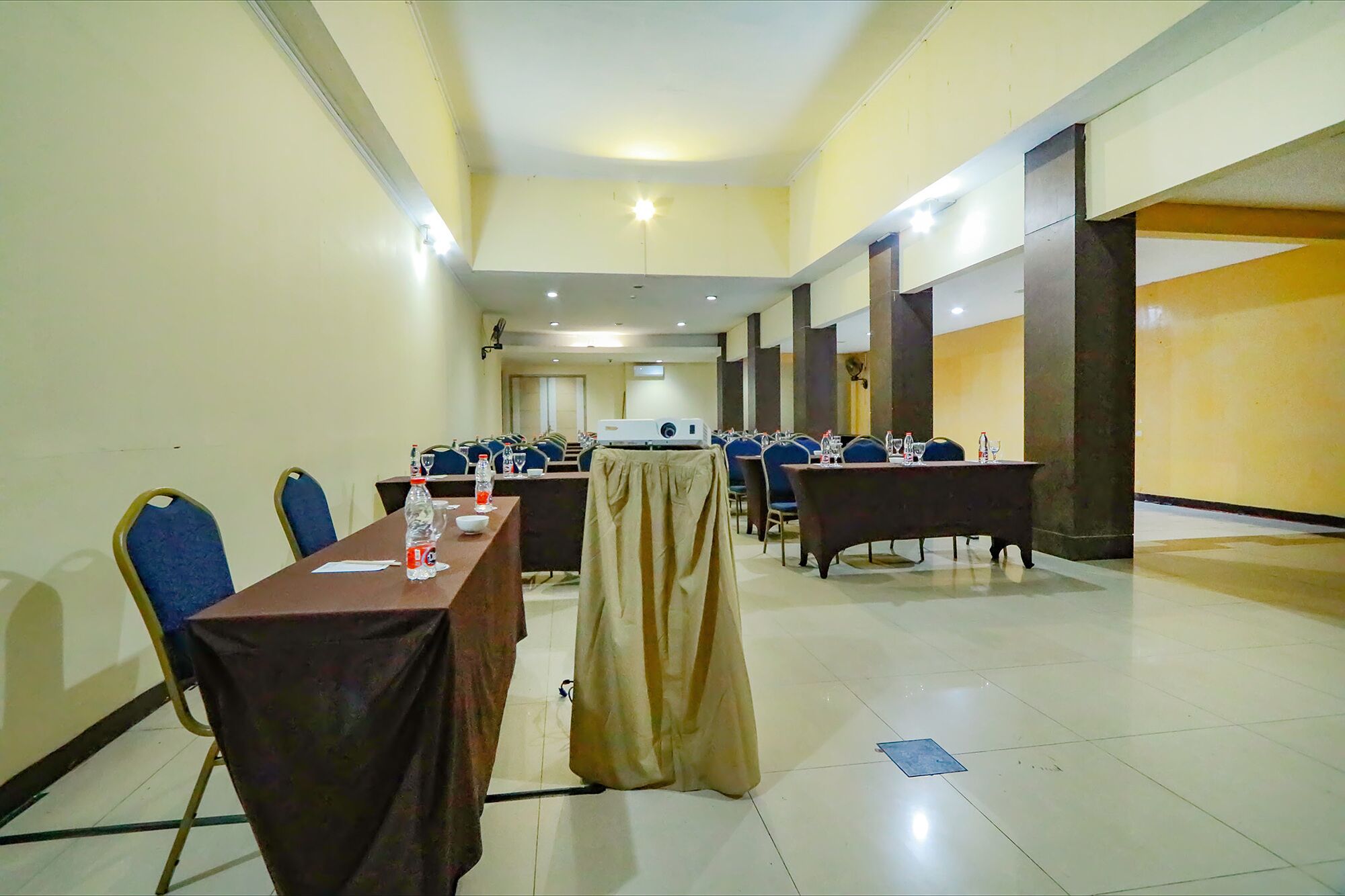 A conference room with multiple tables and chairs, equipped with projectors and water bottles.