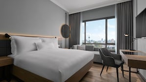 Een moderne hotelkamer met een groot bed, een bureau en een stoel. Grote ramen bieden uitzicht op de stad.