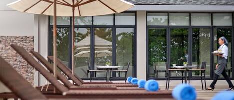 A pool area with lounge chairs and umbrellas, a dining area with tables and chairs, and a person walking by.