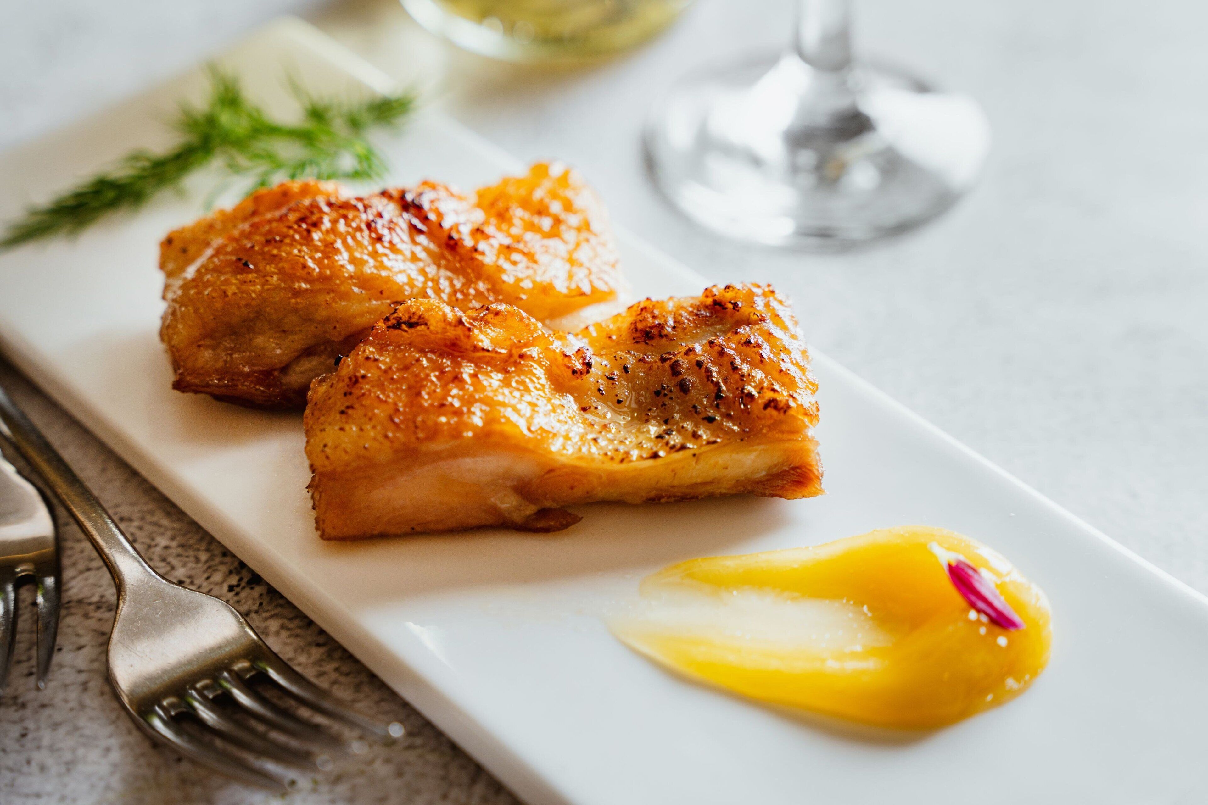 A white plate with grilled chicken and a lemon slice.
