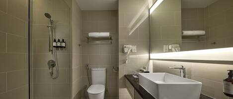 Un baño moderno con ducha envuelta en vidrio, inodoro blanco, tocador con lavamanos grande y espejo sobre el lavamanos.