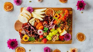 Una tabla de embutidos con diversos quesos, carnes, frutas y flores sobre una tabla de madera.