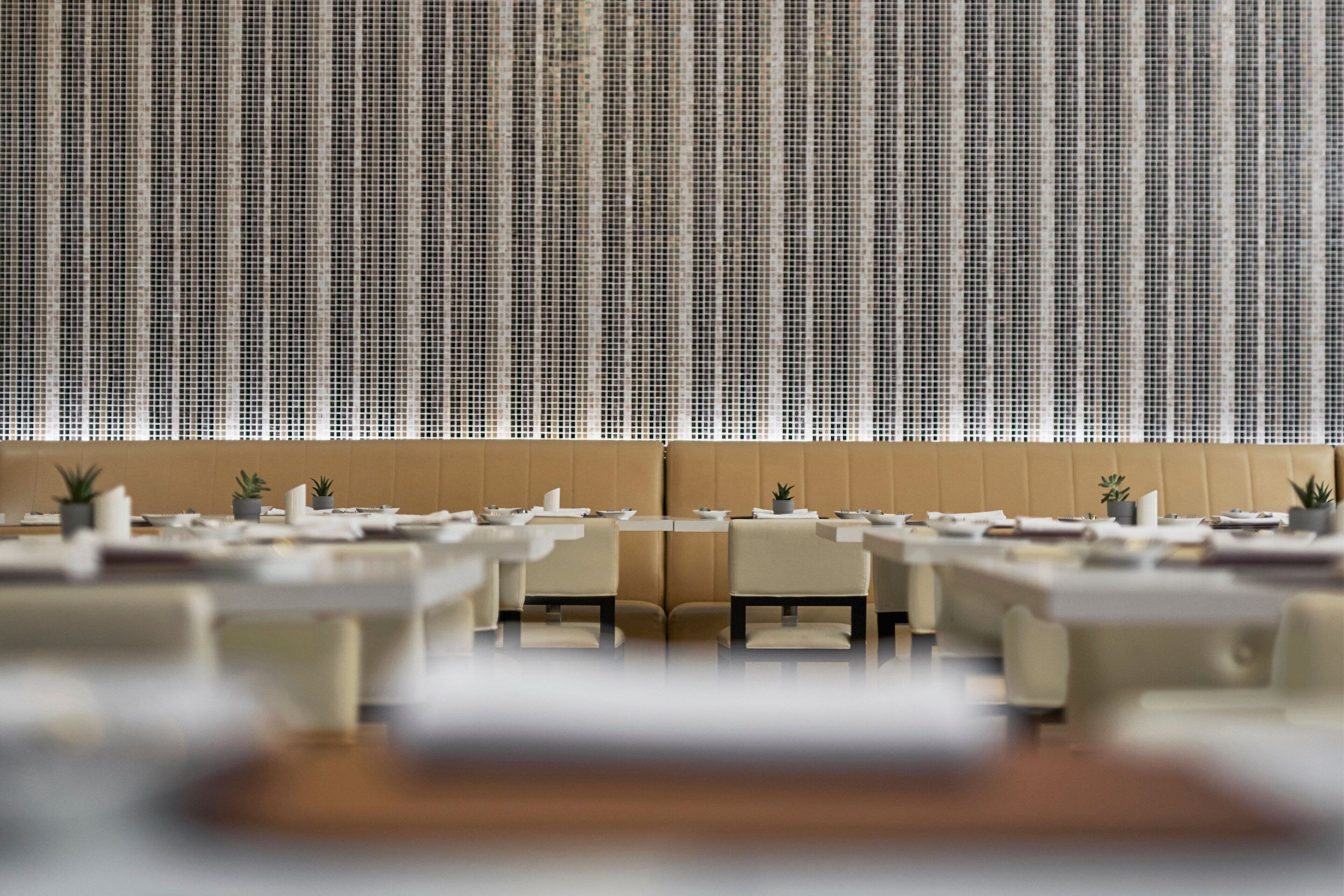 A modern dining area with a long table and chairs, a high ceiling with a patterned wall, and a cushioned bench area.