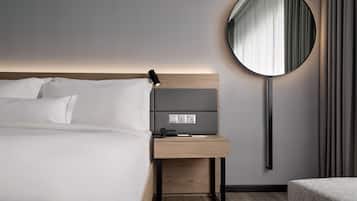 Una habitación de hotel moderna con una cama bien hecha, una mesita de noche con lámpara, un espejo redondo y un enchufe.