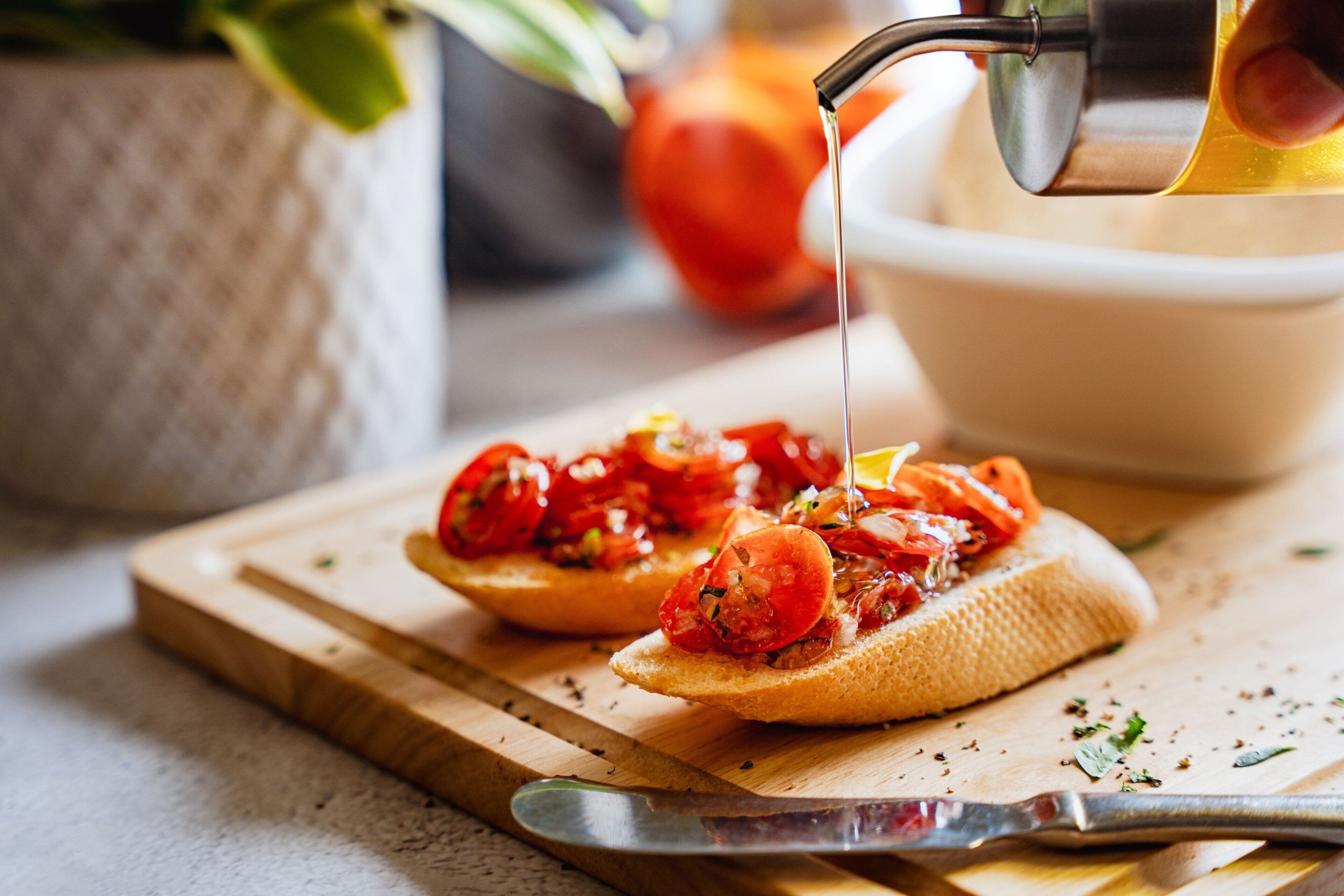 Two pieces of toast topped with tomatoes and herbs, with a knife and a bowl on a wooden cutting board.