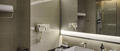 A modern bathroom with a large mirror, a white sink, and a shower area.
