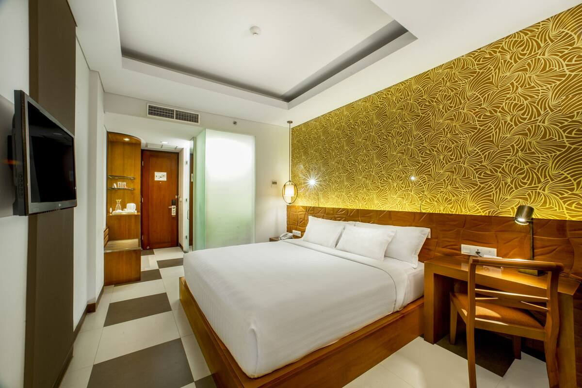 Ein Hotelzimmer mit einem großen Bett, einem Schreibtisch mit Stuhl, einem Fernseher und einer Wand mit Muster.