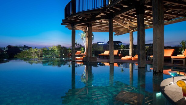 A clear infinity pool with wooden deck seating and a view of the city skyline. - Sun Island Hotel & Spa Legian (Kuta)