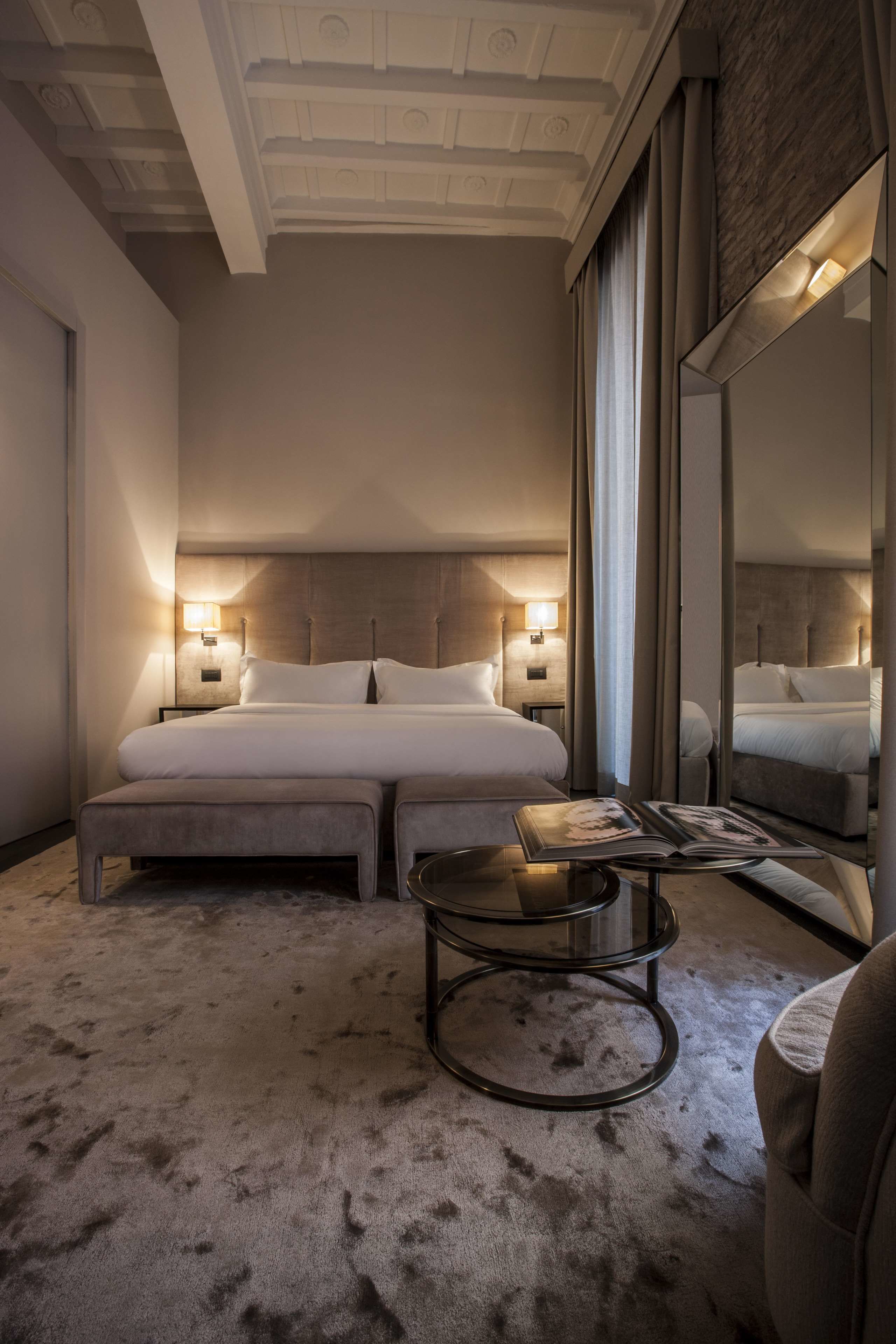 Une chambre d’hôtel avec un grand lit, deux tables de chevet avec des lampes, une table basse ronde et un grand miroir.
