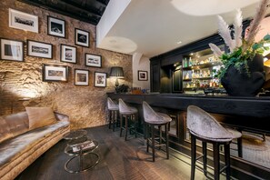 A bar area with a stone wall, framed pictures, a bar counter, and stools.