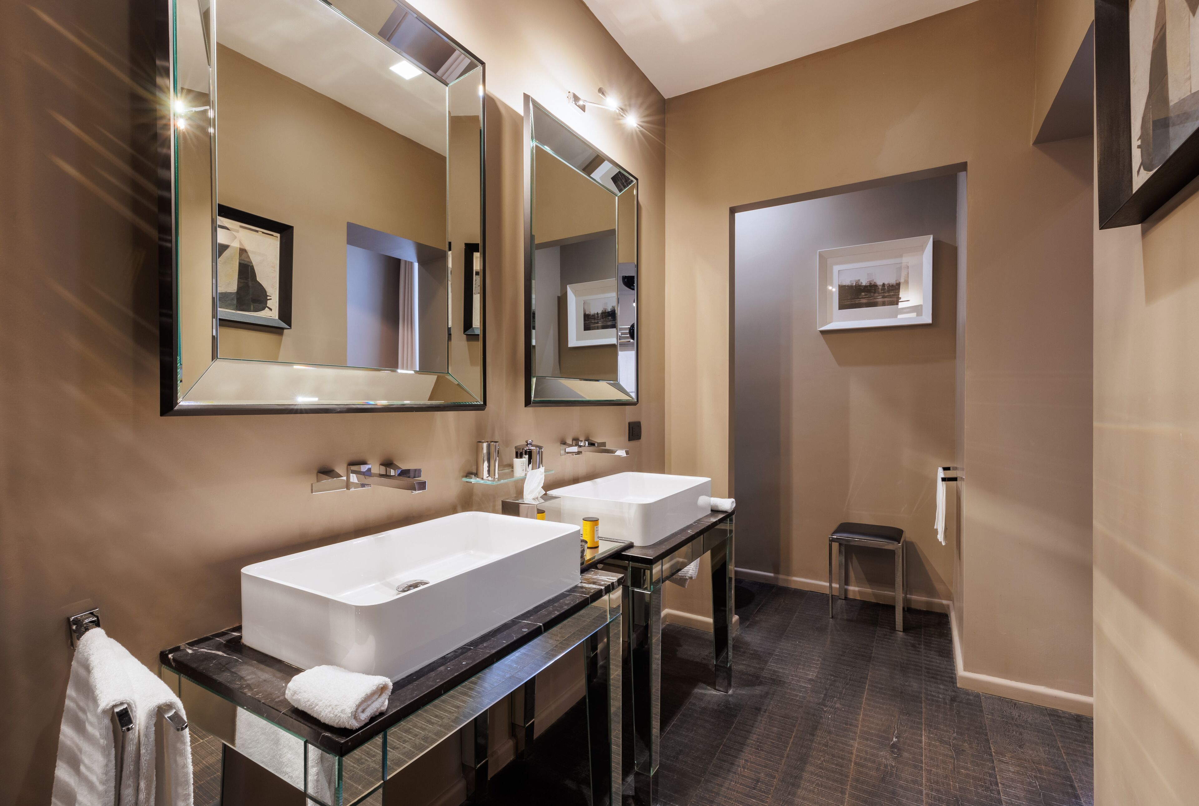 A modern bathroom with two sinks, a large mirror, and a small stool.