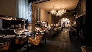 A cozy, dimly lit lounge area with leather sofas and armchairs, a long wooden table, and a chandelier. - DOM Hotel (Rome)