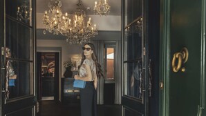A woman in a room with a chandelier, a door with a brass handle, and a blue handbag. - DOM Hotel (Rome)