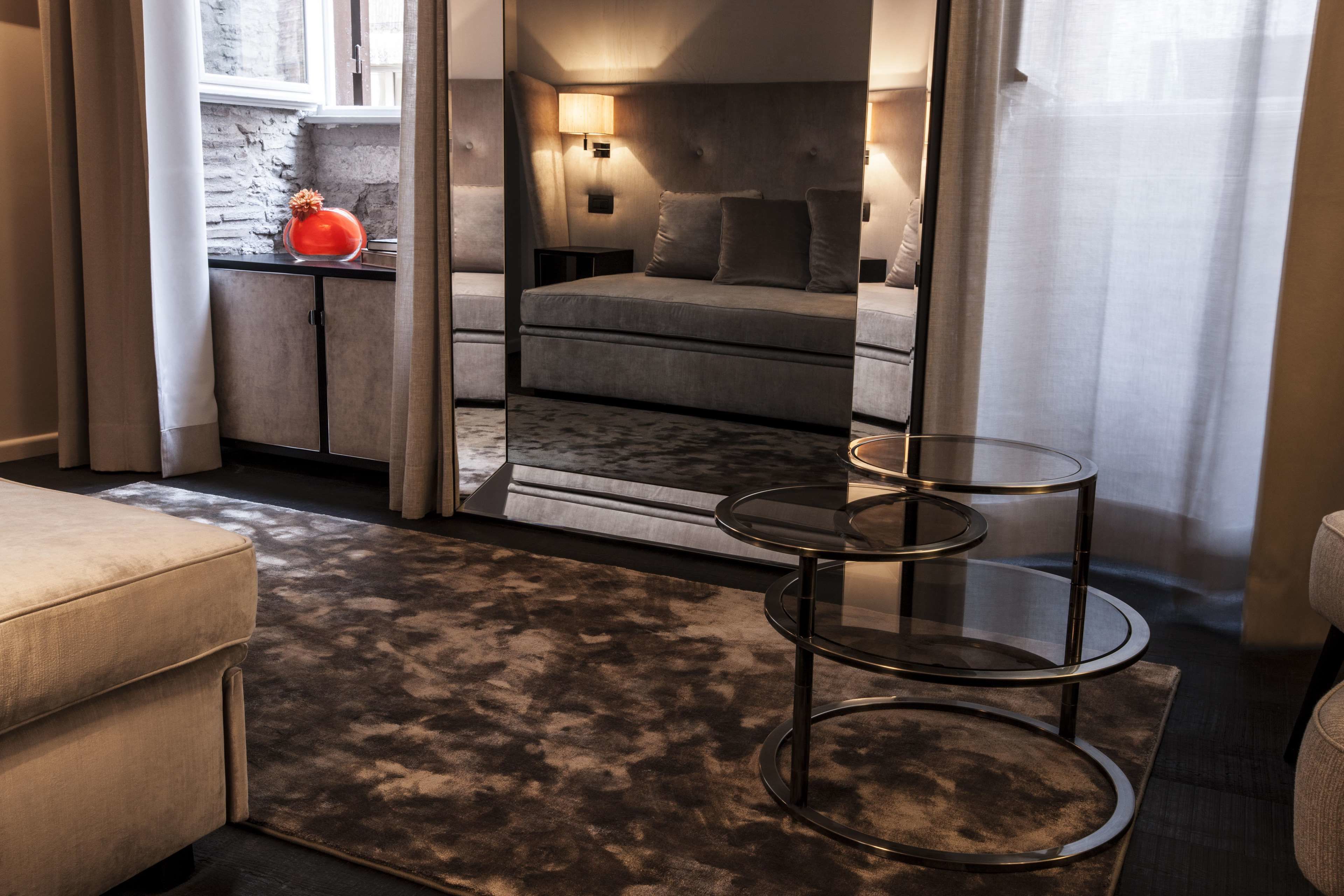 Quarto moderno com sofá cinza, mesa de vidro e vista para a paisagem urbana através de uma janela.