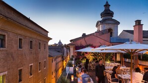 A rooftop terrace with outdoor seating, a view of the cityscape, and a dome structure in the background. - DOM Hotel (Rome)