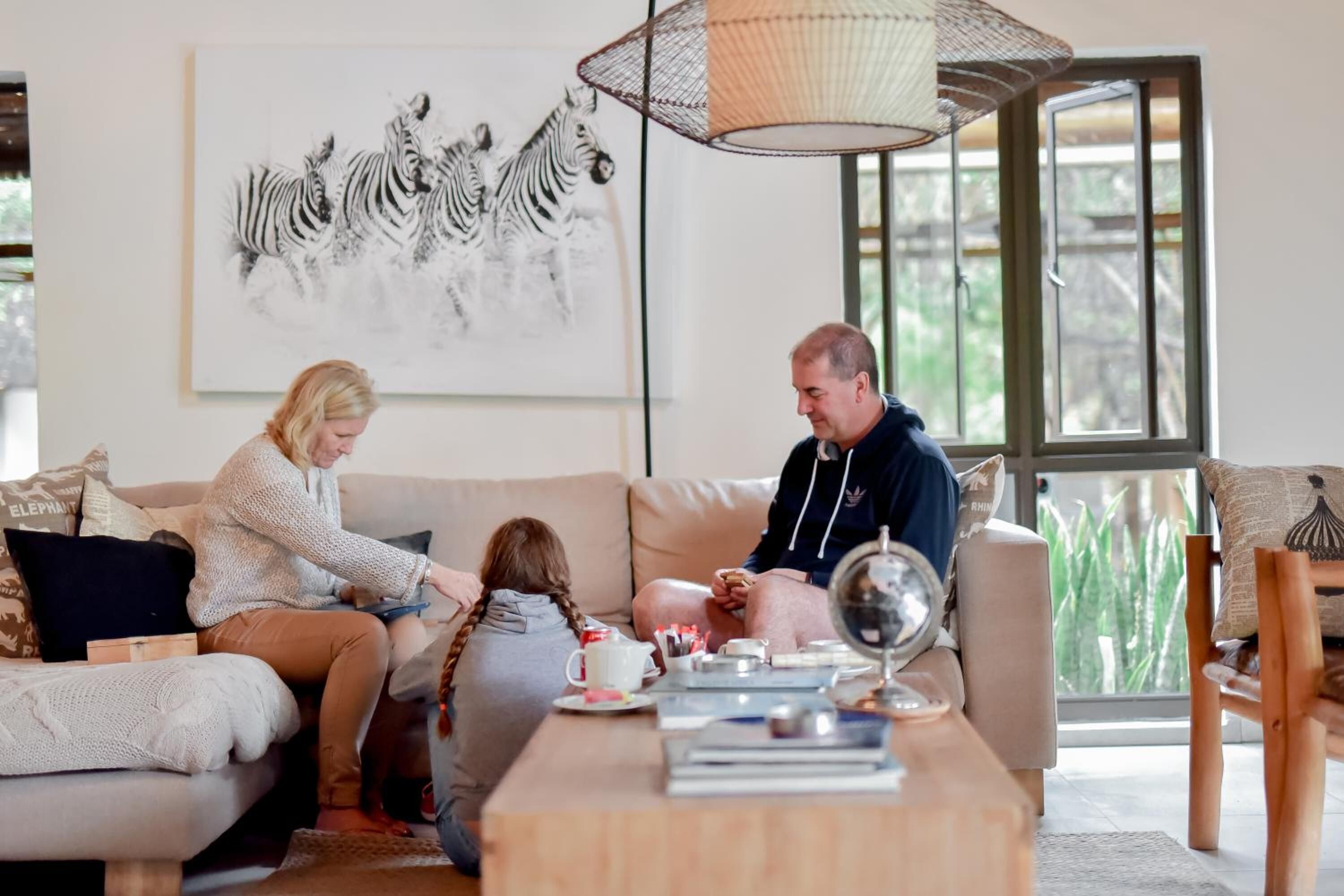 A living room with a sofa, a coffee table with books, a zebra artwork on the wall, and a window with a view of greenery.