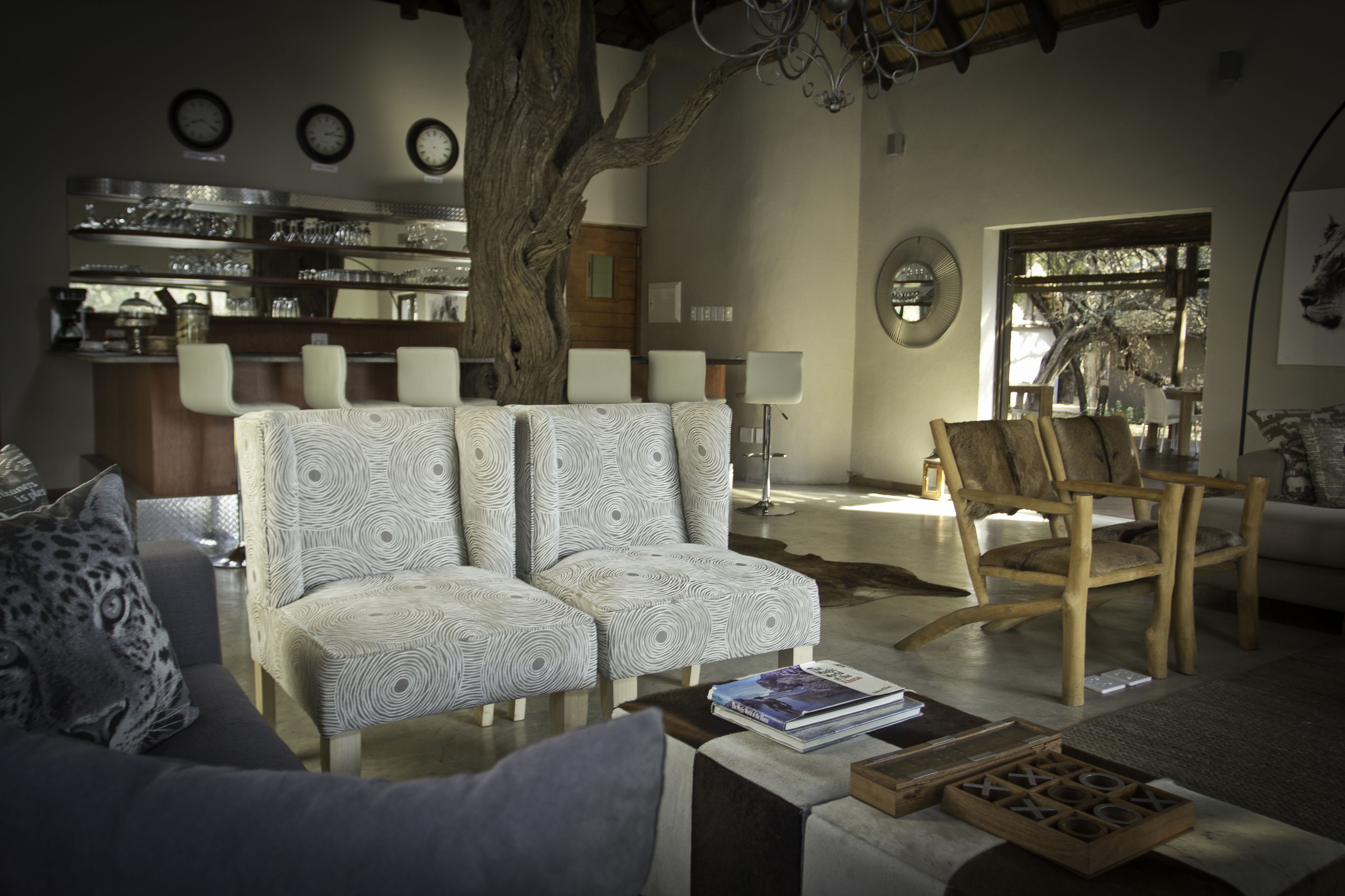 A cozy living room with a large tree, a bar area with shelves of glasses, and a wooden chair.