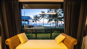 Um sofá de vime com almofadas amarelas em um quarto com vista para uma praia e palmeiras.