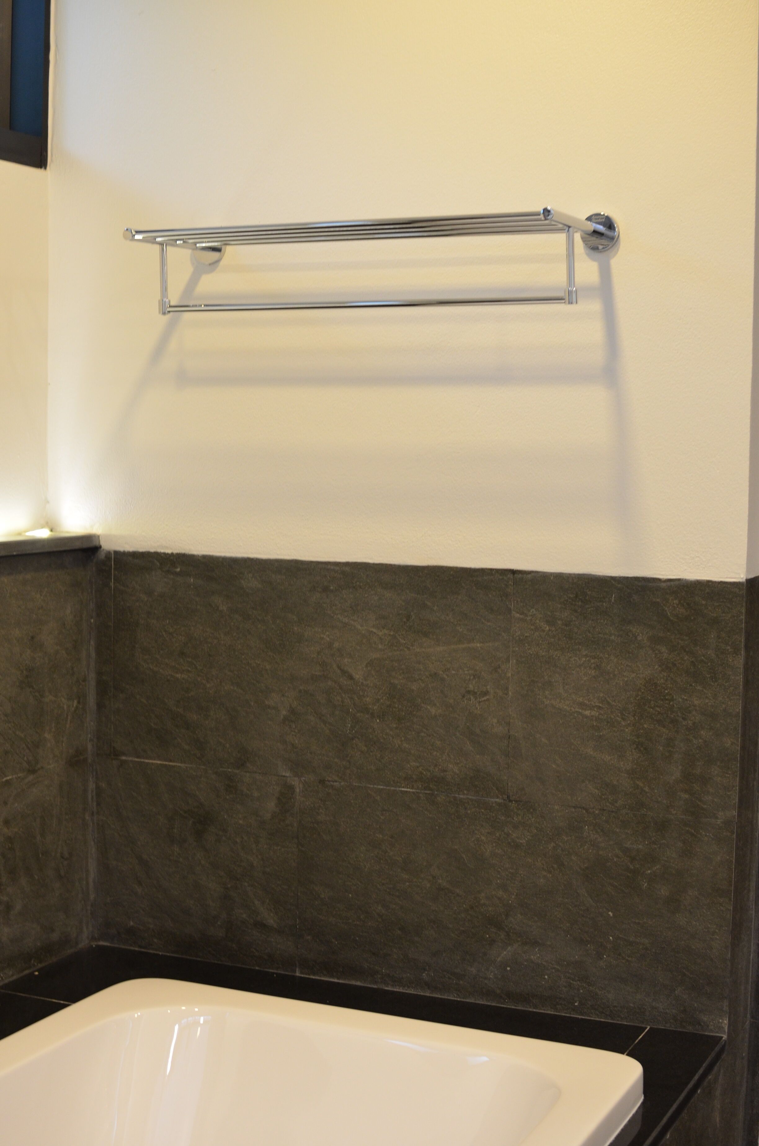 A bathroom with a white bathtub, a chrome towel rack, and dark tiled walls.