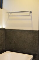 Un baño con una bañera blanca, un perchero cromado y paredes cubiertas de baldosas oscuras.