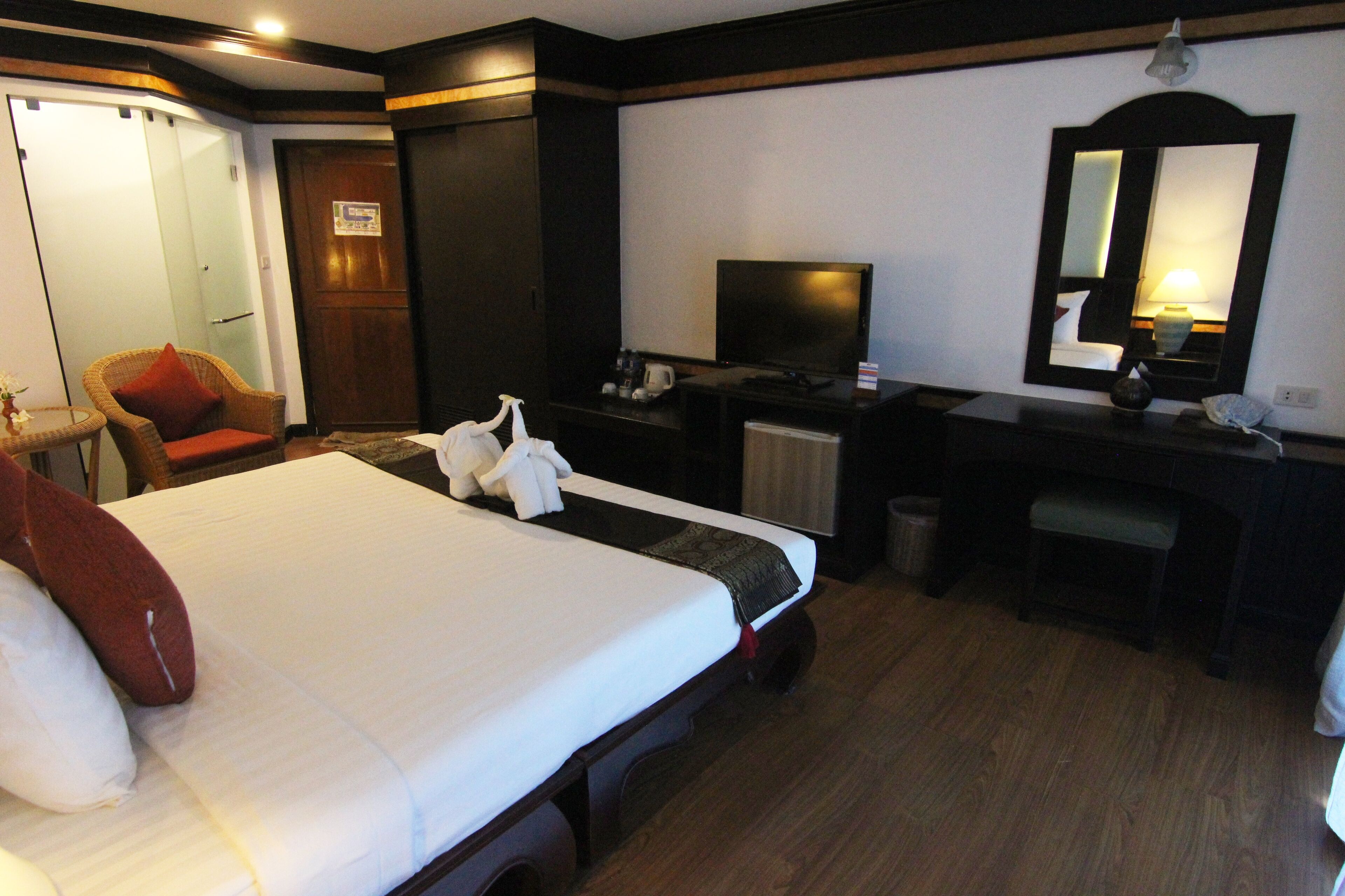 Una habitación de hotel con cama, escritorio, televisión, espejo y armario.
