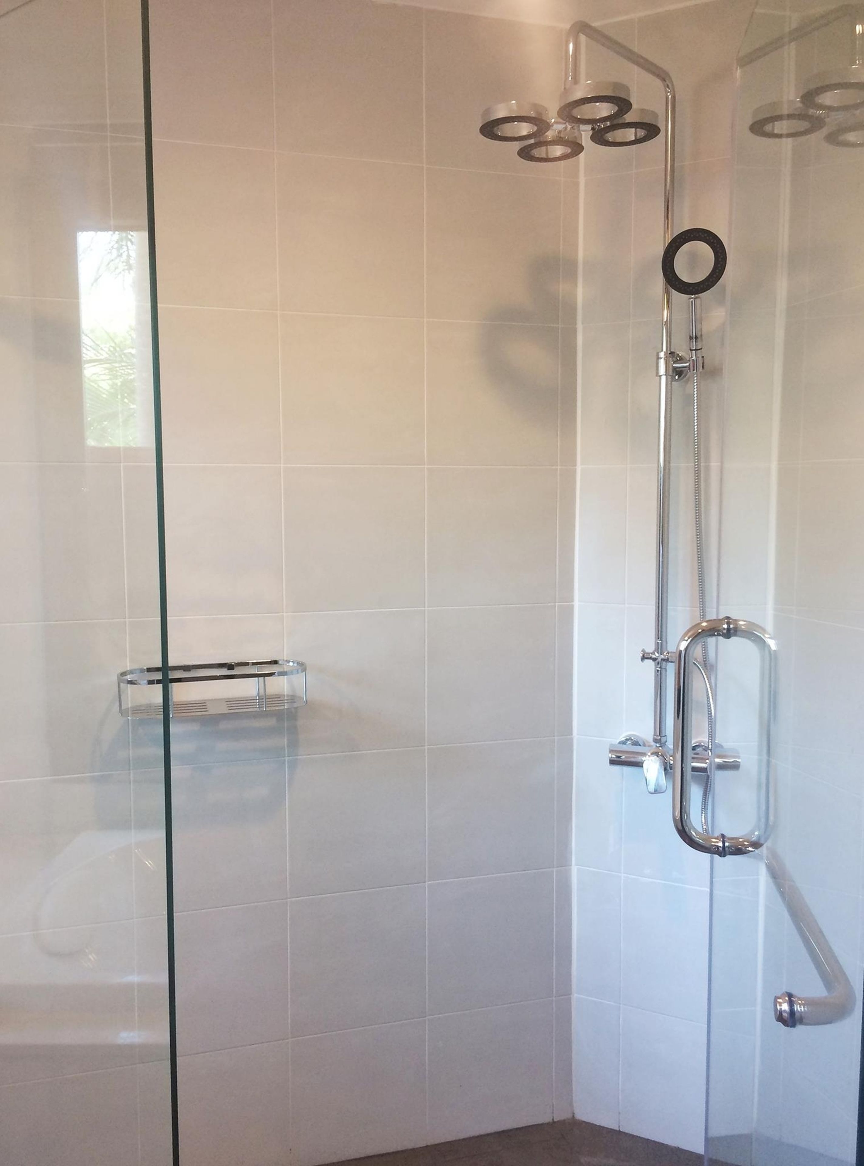 Ducha con mampara de vidrio, cabezal de ducha y panel de control cromados.