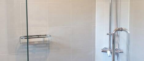 Ducha con mampara de vidrio, cabezal de ducha y panel de control cromados.